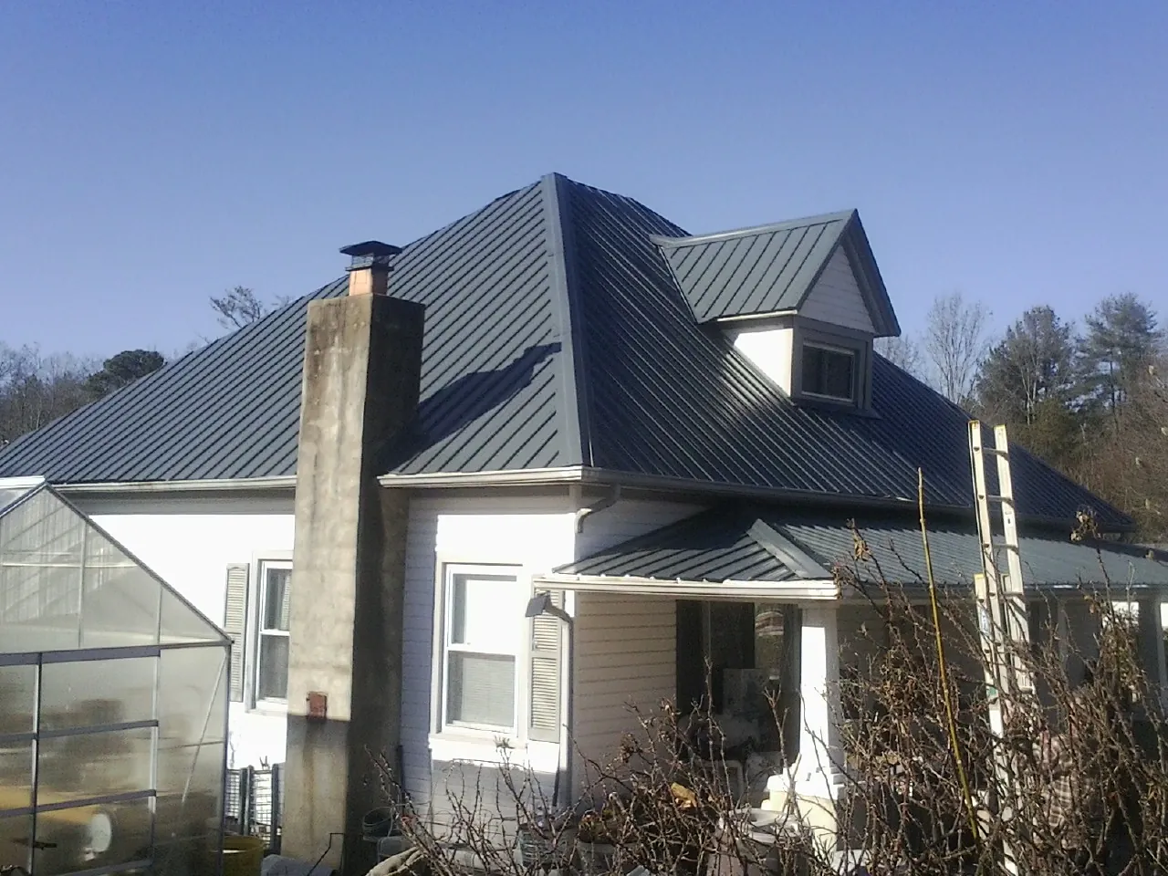 Dark blue standing seam metal roof on a white farmhouse with dormer — Slate & Tile Roof Repair by Roofing Brothers in Thrall