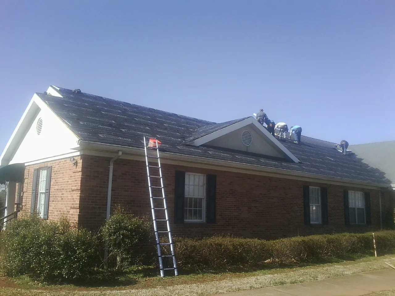 Crew tearing shingles off a brick ranch roof with a ladder set — Emergency Roof Repair work by our crew in Thrall