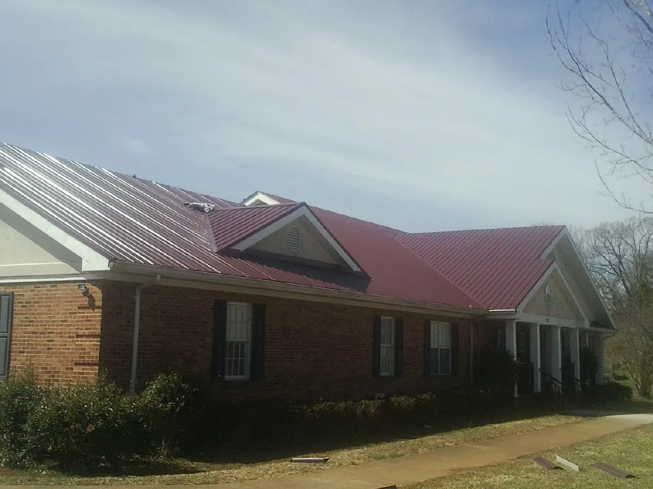 Red metal roof with gabled entries on a long brick building, from a Hail Damage Roof Repair job in Thrall