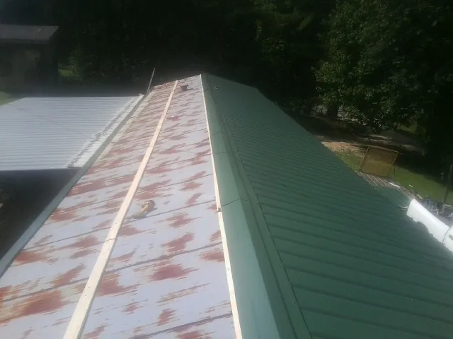 Old rusted panels beside newly installed green metal roofing — Wind Damage Roof Repair by Roofing Brothers in Thrall