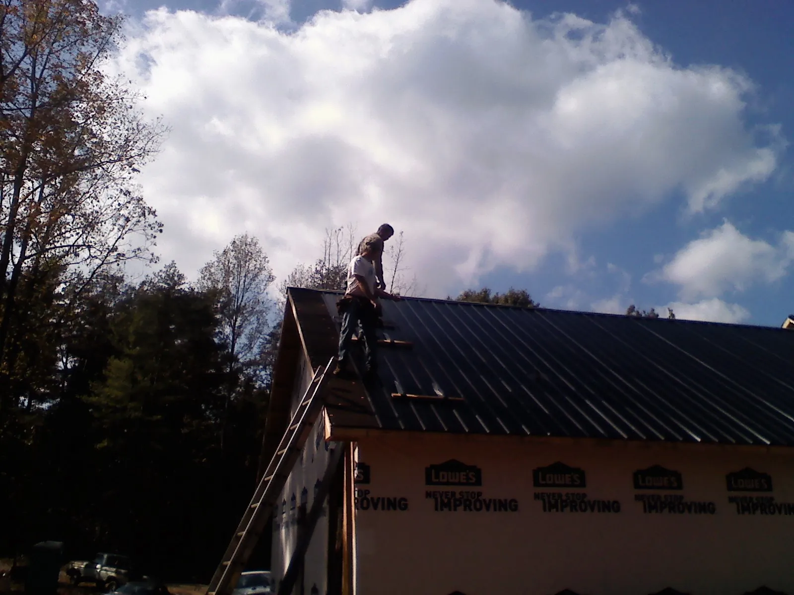 Roofer fastening dark metal panels high against a cloudy sky, from a Roof Inspection job in Thrall