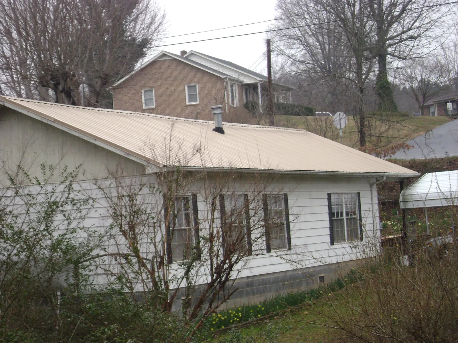 Tan metal roof on a white sided house set into a hillside — Commercial Roofing by Roofing Brothers in Thrall